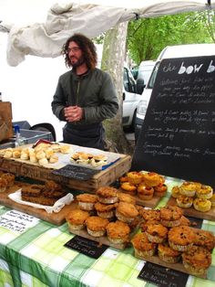 a man standing in front of a table filled with cupcakes and muffins