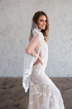 a woman in a white wedding dress with a veil on her head is posing for the camera