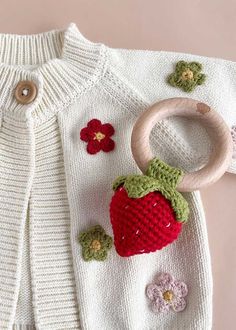 a knitted sweater with flowers and a wooden ring on the front, next to it is a crochet strawberry