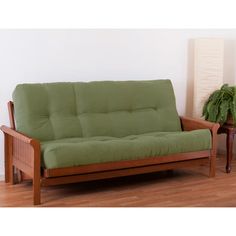 a green futon couch sitting on top of a hard wood floor next to a potted plant