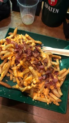 a green plate topped with french fries covered in cheese and bacon