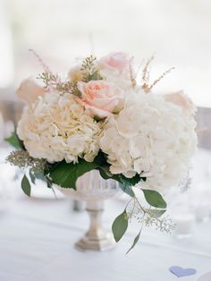 a vase filled with white and pink flowers on top of a dining room table at a wedding