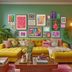 a living room filled with yellow couches and colorful paintings on the wall above them