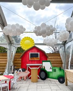 an outdoor party with balloons and farm animals on the floor, including a tractor in front of a red barn