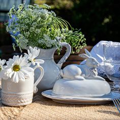 the table is set with white dishes and flowers