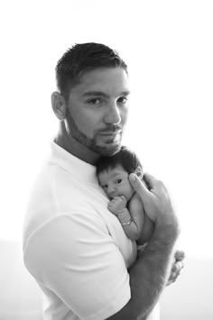 a man holding a baby in his arms while wearing a white shirt and looking at the camera