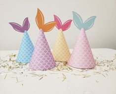 three party hats with mermaid tails on them sitting on top of a table covered in confetti