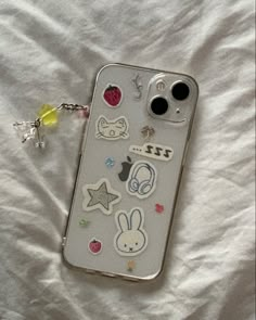 an iphone case with various stickers on it laying on a white sheet next to a keychain