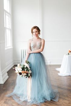 a woman in a blue dress standing on a wooden floor holding a bouquet and looking at the camera