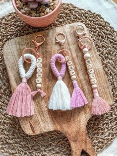 three key chains with tassels are sitting on a wooden board next to a potted plant