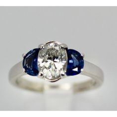 This is part of Chairish’s Fine Jewelry assortment.  Diamond Ring with Half Moon Sapphire Sides  This ring is unusual as it has a center oval cut Diamond of 1.20 carats and enhanced by moon cut Sapphires of 1/2 carat each totaling 2.20 tcw. The ring is sized 6 1/4 and can be enlarged or made smaller. It weighs 4.8 grams. This ring is perfect for a wedding, anniversary, or birthday. The Diamond is a H-I in color and VS2- SI in clarity. The Sapphires are beautiful eye clean and intense Sapphire Bl Oval Brilliant Cut Sapphire Ring, Oval Sapphire Ring With Rose Cut Diamonds For Promise, Platinum Three-stone Oval Rings, Platinum Three Stone Oval Rings, Oval Sapphire Ring In Diamond White, Three-stone Oval Platinum Wedding Ring, Oval Three Stone White Gold Wedding Ring, Oval Sapphire Ring With Center Stone, Three Stone Oval Platinum Wedding Ring