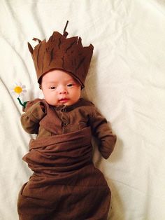 a baby dressed in a brown outfit laying on top of a bed next to a flower