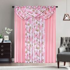 a living room with pink curtains and flowers on the drapes, in front of a gray chair