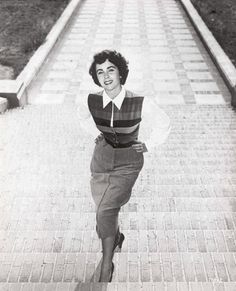 an old black and white photo of a woman walking down a brick path with her hands on her hips