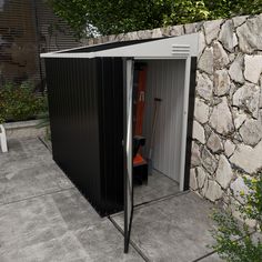 a black and white shed sitting next to a stone wall with an orange umbrella in it