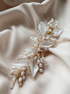 a bridal hair piece with pearls and leaves on it's side, laying on a satin fabric