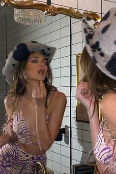 a woman is brushing her teeth in front of a mirror wearing a hat and dress