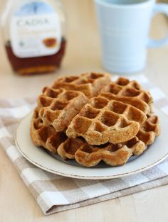 a stack of waffles on a white plate next to a cup of coffee