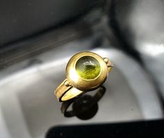 This Unique 18K Gold Peridot Ring is a one-of-a-kind item. It was made in the 1980s so it's a real vintage ring. The style is distinctively Art Deco. It features a 7mm Cabochon Peridot which does have some scuffing but this is really only noticeable from a distance (see close-up photo). The top (dome) of the ring measures 11.5mm and the shank is just over 3mm wide. This ring weighs 5.4 grams. Unique Hallmarked Yellow Gold Emerald Ring, Collectible Yellow Gold Emerald Ring With Cabochon, Collectible Yellow Gold Emerald Cabochon Ring, Classic Gold Ring With Peridot, Vintage Hand Forged Yellow Gold Rings, Unique Gold Emerald Cabochon Ring, Unique Green Sapphire Round Ring, Antique Green Signet Ring, Unique Green Round Sapphire Ring