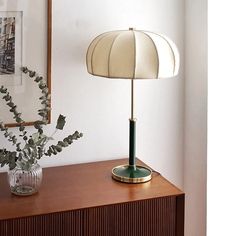 a table lamp sitting on top of a wooden dresser next to a vase with flowers