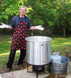 a man in an apron standing next to a large metal pot on a table outside