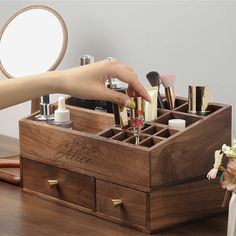 a person's hand reaching into a wooden box with makeup and cosmetics in it