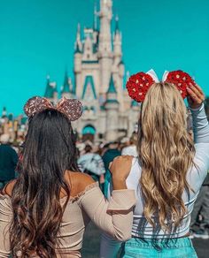 two girls in front of a castle with minnie mouse ears on their heads, looking at the sky