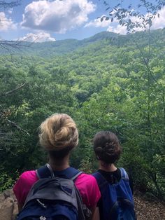 two people with backpacks look out over the mountains and trees on a sunny day