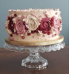 a large cake with pink and red frosting roses on it's side sitting on a glass platter