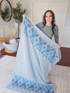 a woman holding up a blue and white crocheted blanket on top of a rug