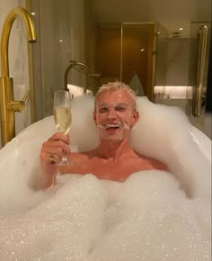 a man in a bubble bath holding a glass of wine and smiling at the camera