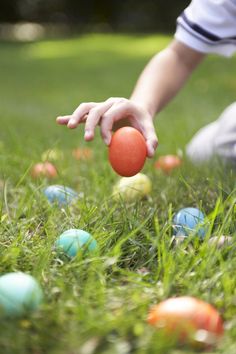 a child reaching for an orange ball in the grass with other colored eggs around it