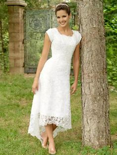 a woman in a white dress standing next to a tree and posing for the camera