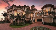 a large house with many windows and palm trees in the front yard at sunset or dawn