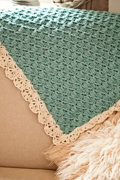 a green crocheted blanket sitting on top of a couch next to a pillow