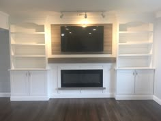 an empty living room with built in bookshelves and a flat screen tv above the fireplace