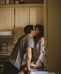 a man and woman kissing in the kitchen while sitting next to each other on the counter