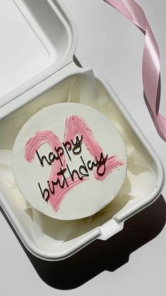 a birthday cake in a white container with pink ribbon on the side and happy birthday written on it