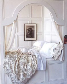 a white bed sitting under a window next to a framed picture on the wall in a bedroom