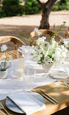 the table is set with white flowers and place settings