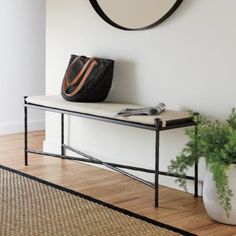 a white bench with a black purse on it next to a wall mounted mirror and potted plant