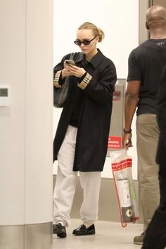 a woman is looking at her cell phone as she walks through an airport terminal with other people