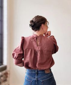 a woman standing in front of a window with her back turned to the camera, wearing a pink blouse and jeans