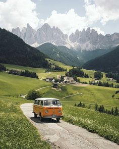 an orange and white vw bus driving down a road in front of some mountains