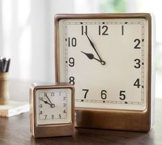 a clock sitting on top of a wooden table next to a pen and pencil holder