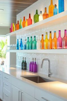 colorful glass bottles are lined up on the wall above the sink in this kitchen area