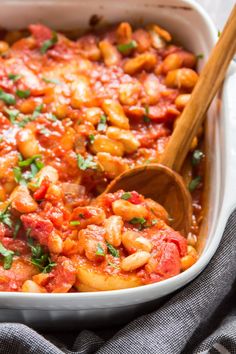 a white casserole dish filled with pasta and tomatoes, garnished with parsley