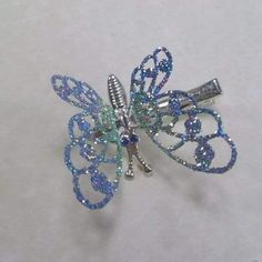 a blue and silver butterfly brooch sitting on top of a white table next to a pair of scissors