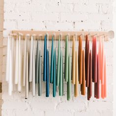 colorful candles are hanging on the wall in front of a white brick wall and wooden rack