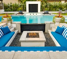 a fire pit surrounded by blue and white couches in front of a swimming pool